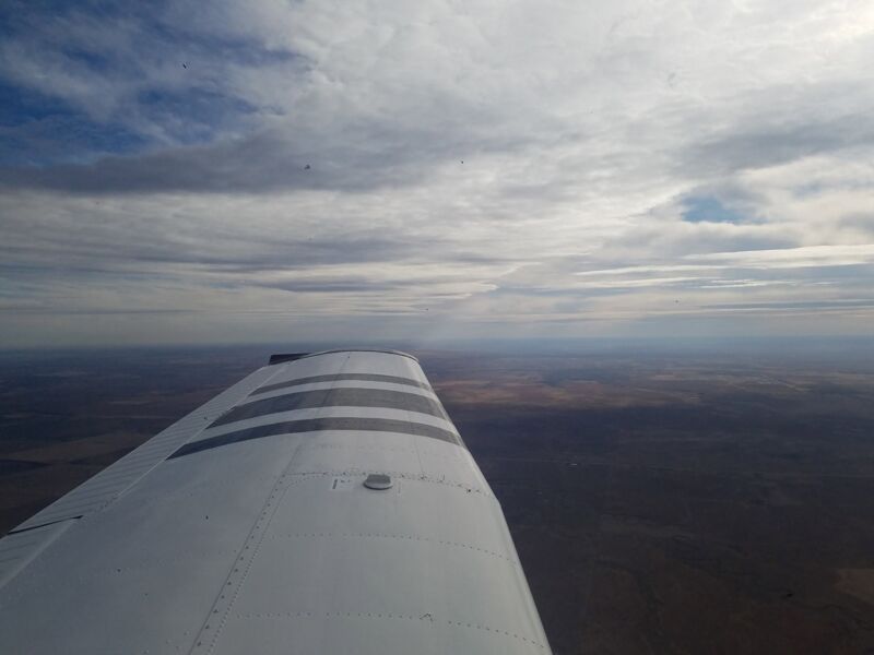 View along the wing over flat country under a broken cloud layer